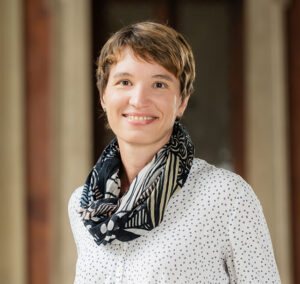 Portraitfoto von einer Frau mit kurzen Haaren, weißer Bluse mit schwarzen Punkten und Halstuch